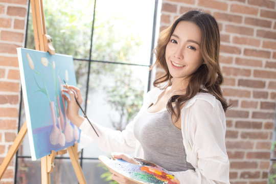 Asian woman paints picture on canvas with oil paints. Woman painting picture with attractive smiling.