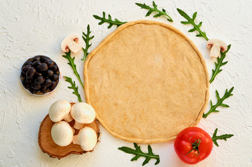 Fototapeta na wymiar Raw pizza dough on the white background with free copy space. Dough with ingredients for vegetarian pizza: mushrooms, black olives, tomato and fresh rucola. Top view