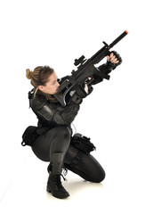 full length portrait of female wearing black  tactical armour, crouching pose holding a weapon, isolated on white studio background.