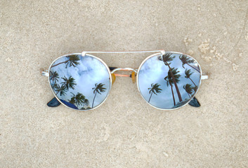 Fototapeta na wymiar Mirrored sunglasses close up on the beach sand with palm trees reflection