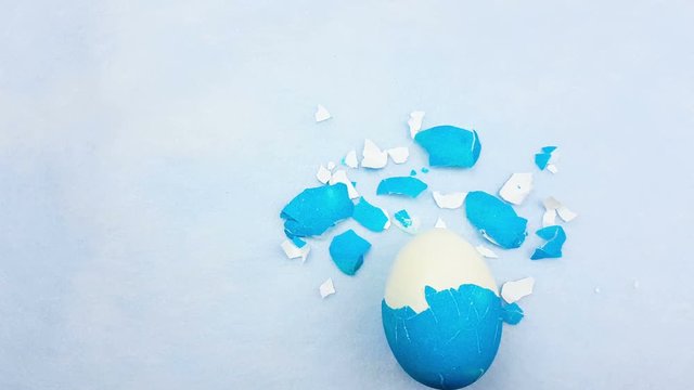 Eggshell with color easter egg on pastel blue background.