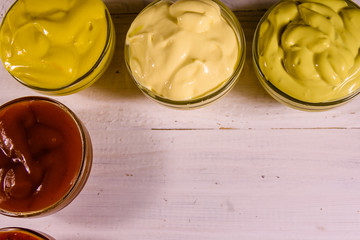 Different sauces in glass bowls on wooden table. Top view