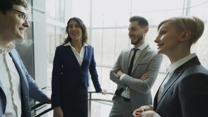 Businesswomen and businessmen colleagues talking in moving elevator and come out from it in modern business center