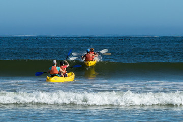 Two double yellow kayaks with four people rowing through the waves in a calm sea