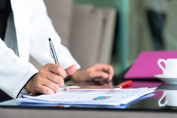 Hand of businesswoman holding with silver pen and playing a phone on documents in the office interrior