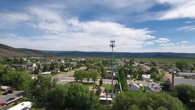 Flying toward cell tower with workers on a lift. 