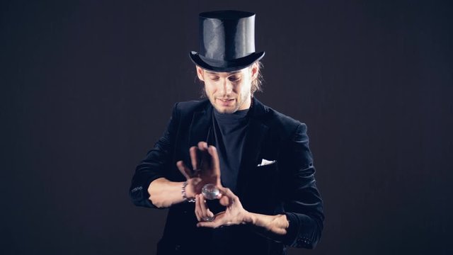 Magician is making a sparkling crystal disappear from his right fist and taking from the air.