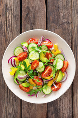 Healthy vegetarian dish, vegetable salad with fresh tomato, cucumber, bell pepper, red onion, avocado and arugula
