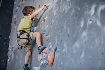 Fototapeten little boy climbing a rock wall indoor. © altanaka