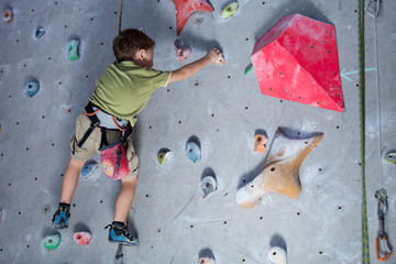 little boy climbing a rock wall indoor.