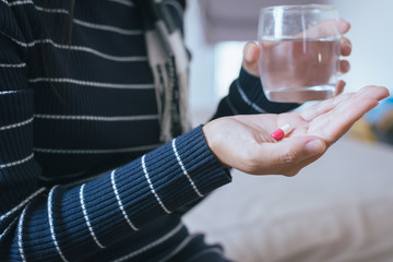 Woman with pills or capsules on hand and a glass of water