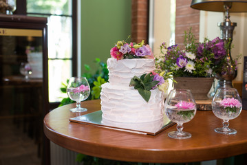 White 2 tiered wedding cake decorated with pink and lilac flowers on the top. Traditional Two Tiered White Wedding Cake with Flowers. Restaurant