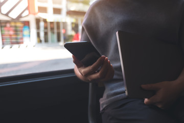 Closeup image of a woman using and looking at a black smart phone while holding laptop computer