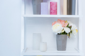 close-up view of white wooden shelves with books, candles and flowers in vase