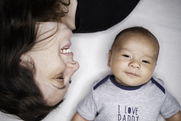 Portrait of beautiful mum playing with her 3 months old baby in bedroom, top view, love mum concept