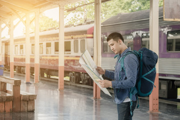 Fototapeta premium Asian traveler man standing on platform and looking at interesting places to travel from paper map at train station.
