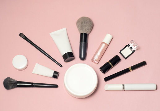 Set of makeup cosmetics, brushes, concealer and other essentials on pink background