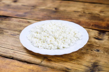 Home made fresh large cottage cheese on white plate on wooden background. Side view.