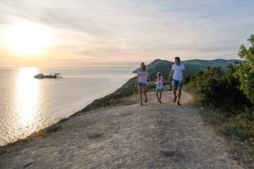 Family mom, dad and son walking down a mountain road with seascape at sunset. Front view.