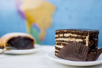 Two different cakes on plates. World map in the background with a blurry background.