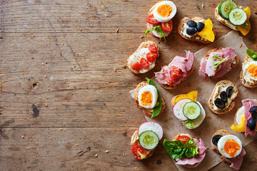 Top view of assorted sandwiches with baguette bread, cheese, ham, eggs, hummus and veggies. Healthy snack on wooden table with copy space.