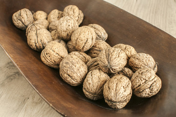 A pile of whole orgranic walnuts in shell closeup in wooden bowl