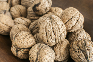 A pile of whole orgranic walnuts in shell closeup on wooden background