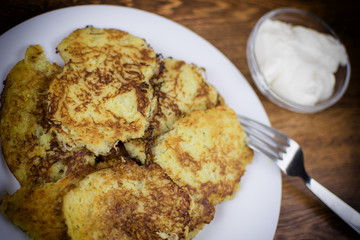 Fried potato pancakes on a white plate and sour cream.