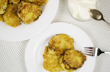 Fried potato pancakes on a white plate and sour cream.