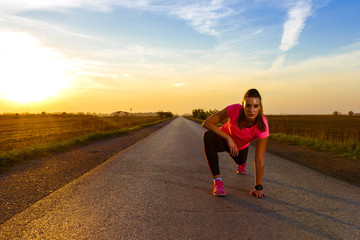 Athletic woman stretching her muscles on rural road during sunset.	