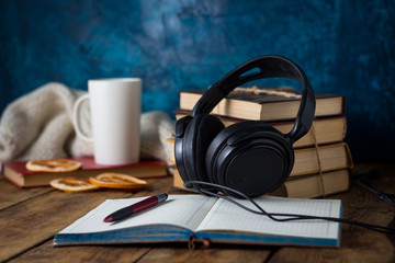 Books are stacked, Headphones, White Cup, Orange Slices, open Diary on a wooden background. The Concept of Audio Books