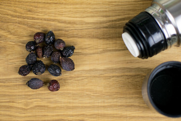 Berries of a dogrose and a thermos on a wooden background.