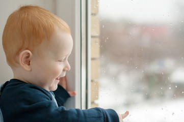 Fototapeta premium Toddler laughs and points finger at the raindrops