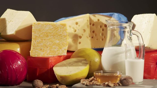 Cheese varieties. Different types of cheeses on wooden table. Stack of cheese wheels, balls and wedges on a dark background. Dolly shot