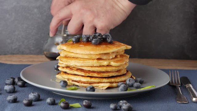 hand adding syrup over a fluffy stack of american style pancakes with blueberries