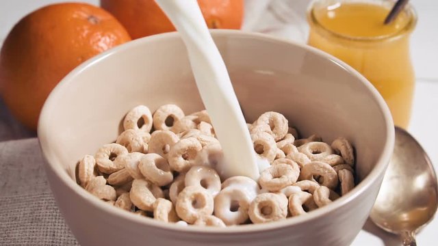 Healthy breakfast of cheerios whole grain cereals with milk, close up. Milk pouring into bowl with honey rings. Pouring milk into a bowl of cornflakes, slow motion.
