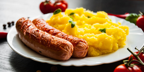 fried meat sausages with mashed potatoes in a plate on dark wooden background