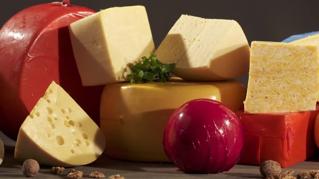 Cheese varieties. Different types of cheeses on wooden table. Stack of cheese wheels, balls and wedges on a dark background. Dolly shot