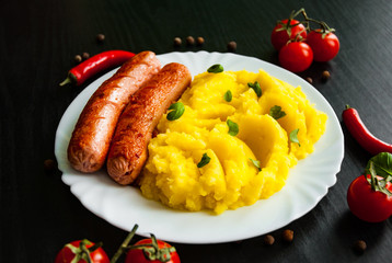 fried meat sausages with mashed potatoes in a plate on dark wooden background