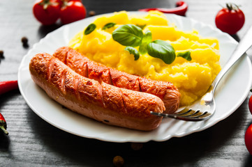 fried meat sausages with mashed potatoes in a plate on dark wooden background