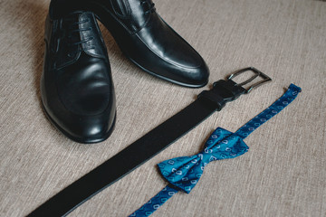 Blue bow tie, leather black shoes and belt. Grooms wedding morning. Close up of modern man accessories