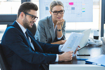smiling businessman and businesswoman looking at documents in office