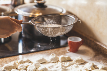 hand sifts flour through sieve over dough pieces