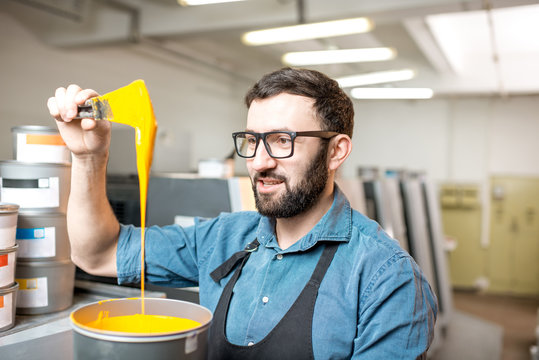 Typographer stiring yellow paint for offset machine standing at the printing manufacturing
