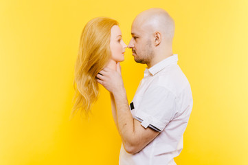 Excited odd bizarre strange unusual sad adult bald hairless man holding plastic blonde woman head. Funny male with girlfriend isolated on yellow. Baldness after chemotherapy. Cancer hair loss concept.