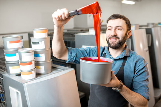 Typographer stiring magenta paint for offset machine standing at the printing manufacturing