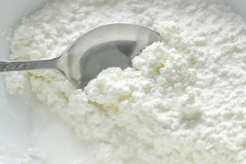 coarse-grained cottage cheese. spoon inserted in cottage cheese