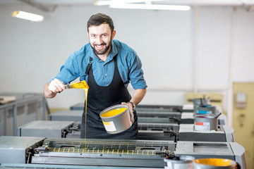 Portrait of a handsome typographer standing with yellow paint for offset machine at the printing...