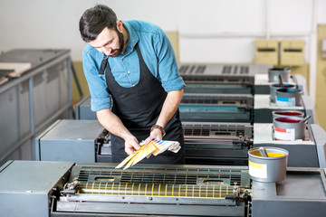Typographer choosing a paint color from pantone swatches standing on the offset printing machine at...