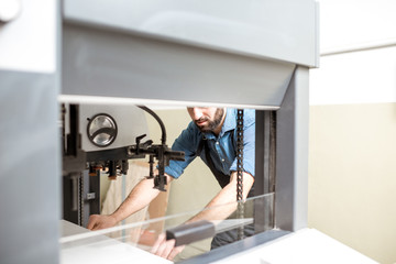Man working with paper sheets feeling into the printing machine at the manufacturing
